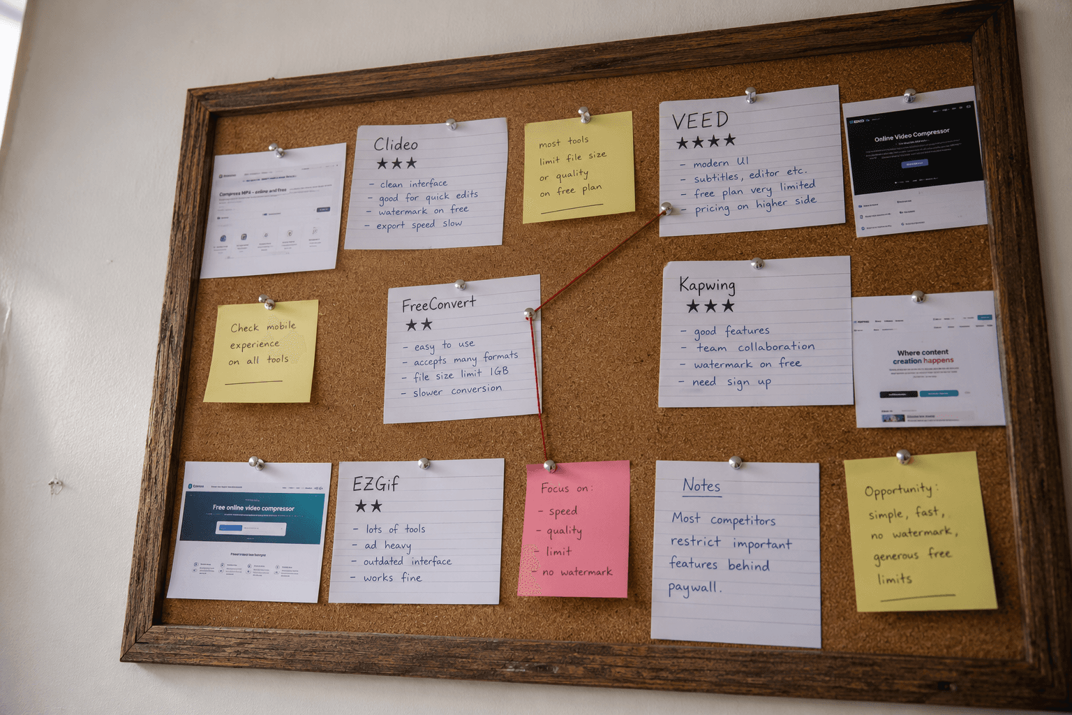A wooden-framed corkboard pinned with handwritten index cards rating Clideo, VEED, FreeConvert, Kapwing and EZGif. Star ratings drawn in ballpoint pen, sticky notes with handwritten comments, printed screenshots of each tool pinned alongside, red string loosely connecting two cards.
